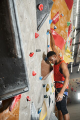 vertical shot of african american man hanging on his fingers on rock wall and looking down