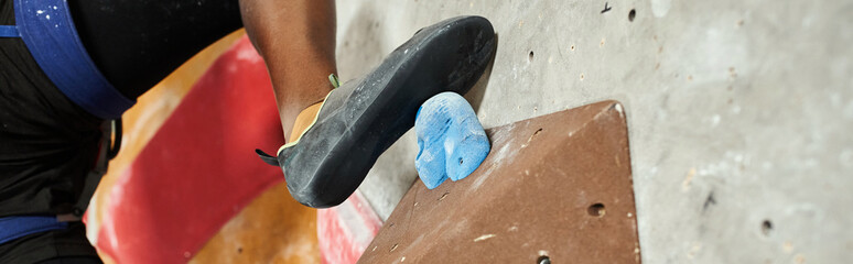 cropped view of foot of athletic young african american man on boulder on climbing rock wall, banner