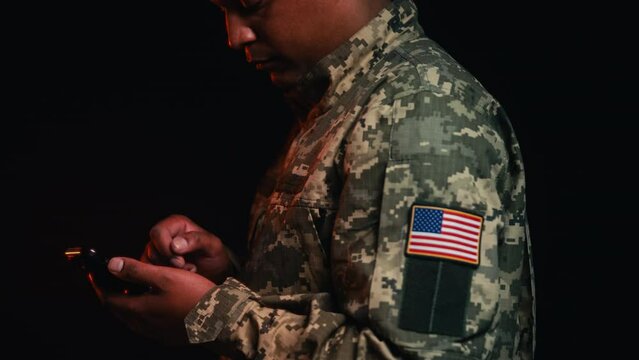 American soldier scrolling smartphone on black background, USA patch on uniform
