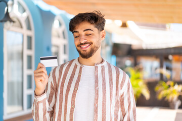 Handsome Arab man holding a credit card at outdoors with happy expression