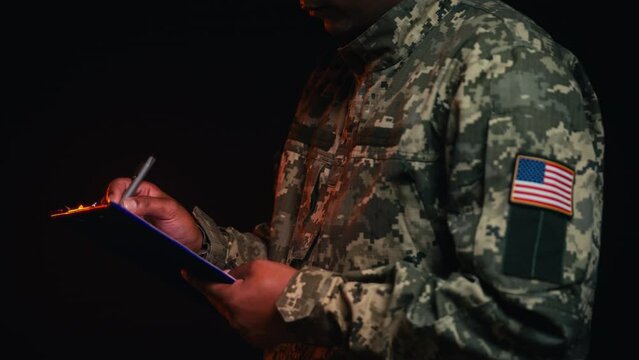 Military man with USA flag patch on sleeve writing in document, office work