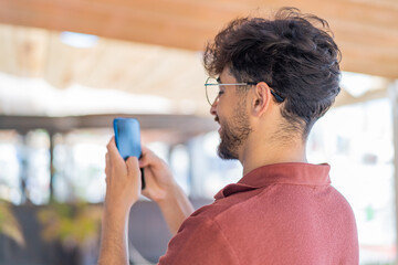 Young Arabian handsome man using mobile phone at outdoors in back position