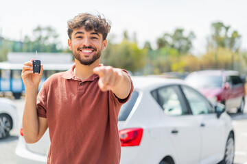 Young Arabian handsome man holding car key at outdoors points finger at you with a confident expression