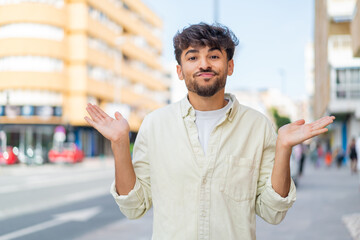 Young Arabian handsome man at outdoors having doubts while raising hands