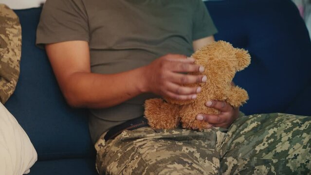Soldier sitting on couch, hugging toy bear, military man missing child and home