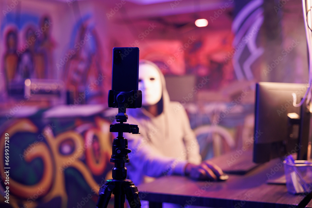 Poster anonymous criminal recording scam on smartphone camera in abandoned warehouse. hacker with hidden id