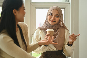 Attractive muslim woman holding paper cup and talking with her colleague during coffee break - obrazy, fototapety, plakaty