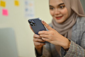 Smiling young muslim woman in hijab using mobile phone at her workplace