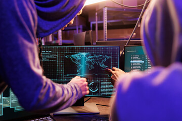 Hackers using spyware on computer screen while working together. Two criminals in hoods cracking password and checking confidential information on internet server in hideout