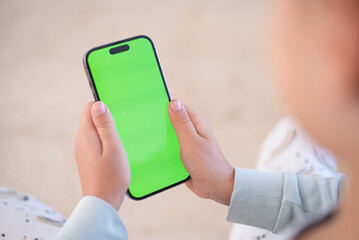 Children’s hands hold phone with green screen. Kid hold phone by two hands. Light background.