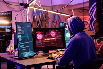 Criminal in hood successfully hacking into computer system in abandoned warehouse. Hacker gaining unauthorized access and stealing valuable data from database online server