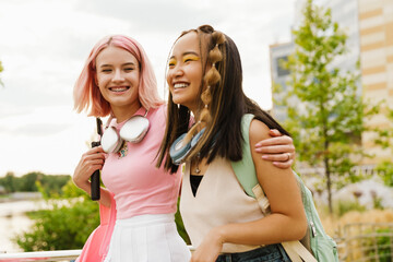 Two cheerful girls hugging while walking together in park - obrazy, fototapety, plakaty