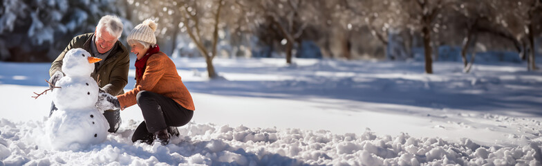 Senior couple out in the snow building a Snowman. Concept of active living for mature and elderly people. Shallow field of view with copy space.