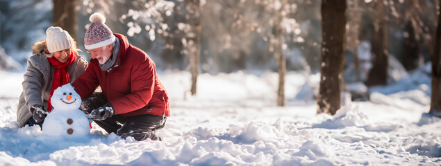 Senior couple out in the snow building a Snowman. Concept of active living for mature and elderly people. Shallow field of view with copy space.