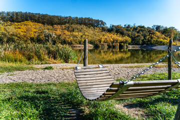 Wooden hammock in a public autumn park on the shore of a pond