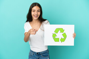 Young French woman isolated on blue background holding a placard with recycle icon and pointing to the front