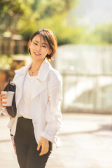 햇빛이 비치는 공원에서 검정 가방을 겨드랑이에 끼고 한손으로 커피를 든...