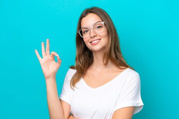 Young caucasian woman isolated on blue background With glasses and doing OK sign
