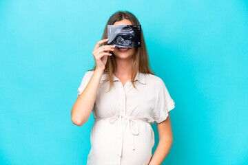 Young caucasian woman isolated on blue background pregnant and holding an ultrasound