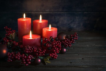 Dark red advent decoration with for lit candles, berrie decoration and Christmas balls against a...