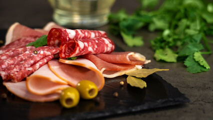 Fresh slices cold cuts, sausage ham bacon jamon on stone cutting board with olives on background of...