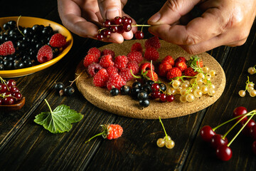 The process of preparing a berry drink from fresh fruits on the kitchen table at home. The chef hands sort the berries. Advertising space on a black background.