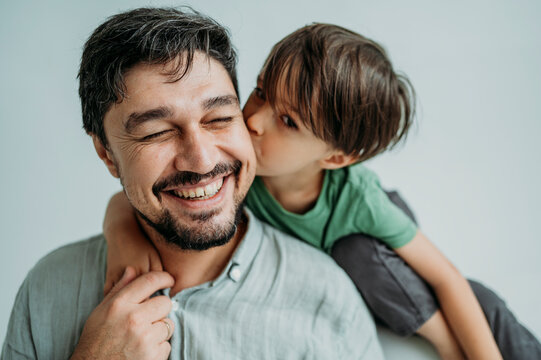 Son kissing happy father on cheeks against white background