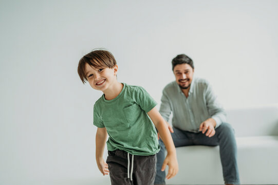 Smiling son with father sitting on sofa near white wall