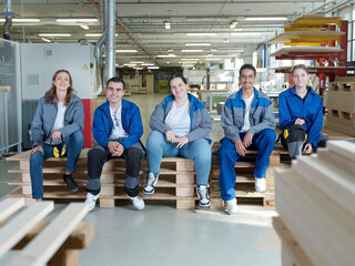 Smiling apprentices sitting on pallets at workshop