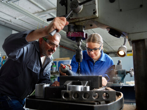 Trainee spraying lubricant on drill bit with instructor at workshop