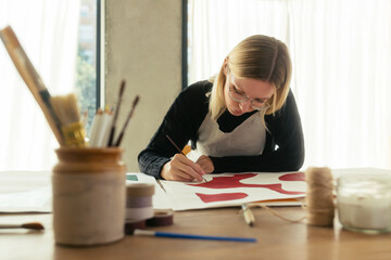 Blond artist painting on canvas at desk in studio