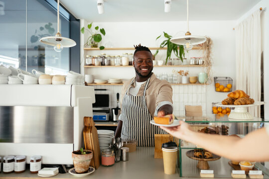 Smiling barista giving pastry to customer at coffee shop