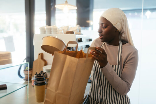 Barista packing food container in paper bag at coffee shop