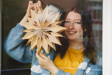 Smiling girl holding star shaped Christmas decoration seen through glass
