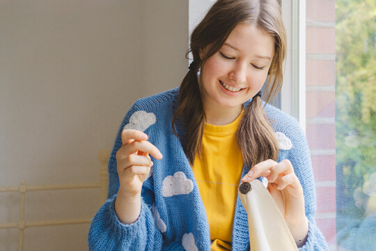 Smiling teenage girl sewing button on clothing