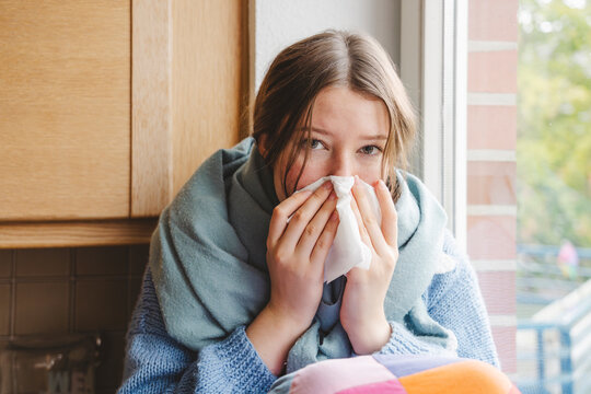 Teenage girl blowing nose on tissue at home