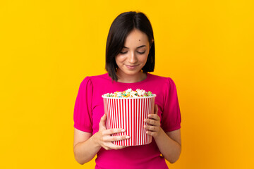 Young caucasian woman isolated on yellow background holding a big bucket of popcorns © luismolinero