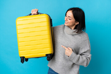 Young caucasian woman isolated on blue background in vacation with travel suitcase