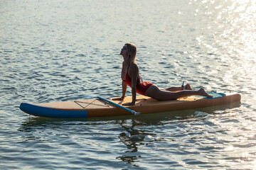 Woman practicing yoga on sup board on sea water.