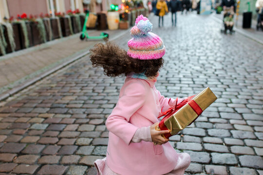 Happy girl holding gift box and running on street
