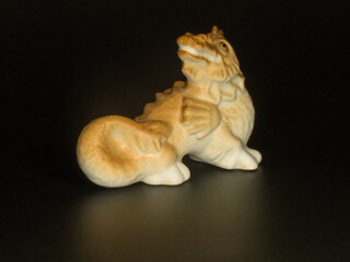 Porcelain figurine of a dragon on a black background with a light reflection.
