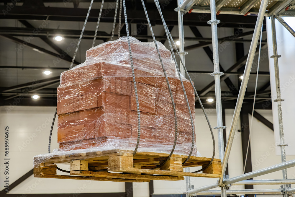 Poster pallet with cargo hangs in air. process of lifting cargo inside hangar. pallet with building blocks 