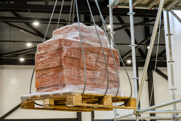 Pallet with cargo hangs in air. Process of lifting cargo inside hangar. Pallet with building blocks...