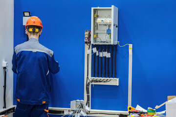 Man electrician at work. Guy fixes electrical equipment. Wall with electrical panel near builder....