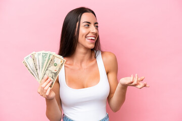 Young caucasian woman taking a lot of money isolated on pink background with surprise facial...