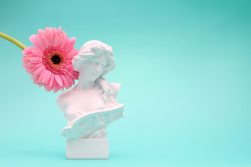 Female bust sculpure greek style with gerbera flower on blue background