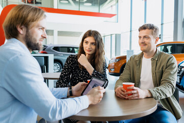 A car dealership manager advises a young couple before buying a new family car at a dealership.