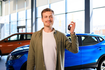 A bearded handsome man with a key to a new car on the background of a dealership. Successful businessman.