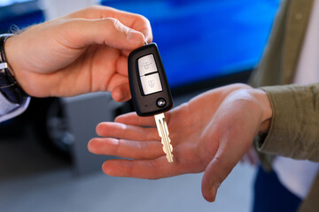 Close-up of the hands of the seller who is handing over the car key to the buyer against the background of cars in the showroom.