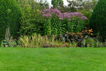 Fototapeta na wymiar Scenic view of a beautiful English style landscape garden with a green mowed grass lawn and a colourful flower bed